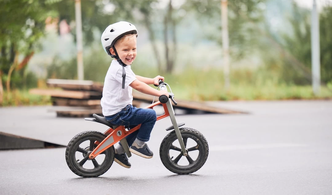 Nasmejano dete vozi svoj prvi bicikli u parku.
