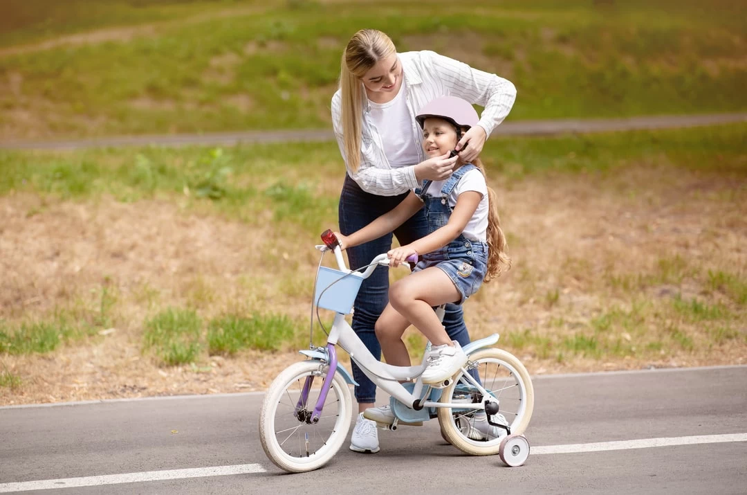 Mama uci cerku da vozi bicikli sa pomocnim tockovima u prirodi.