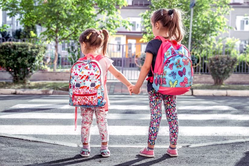 Dve devojčice idu u školu i obe nose ranac na leđima.